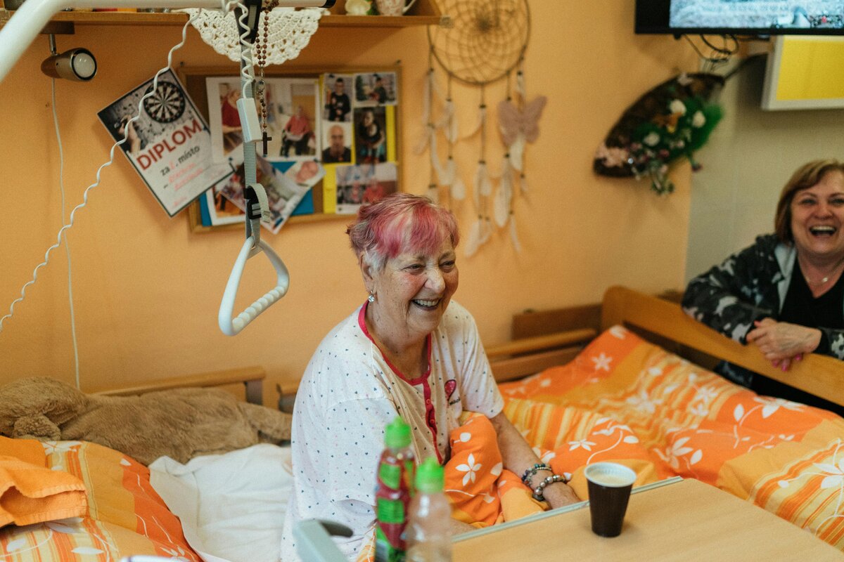 Résidente souriante aux cheveux roses dans sa chambre personnalisée, partageant un moment de joie