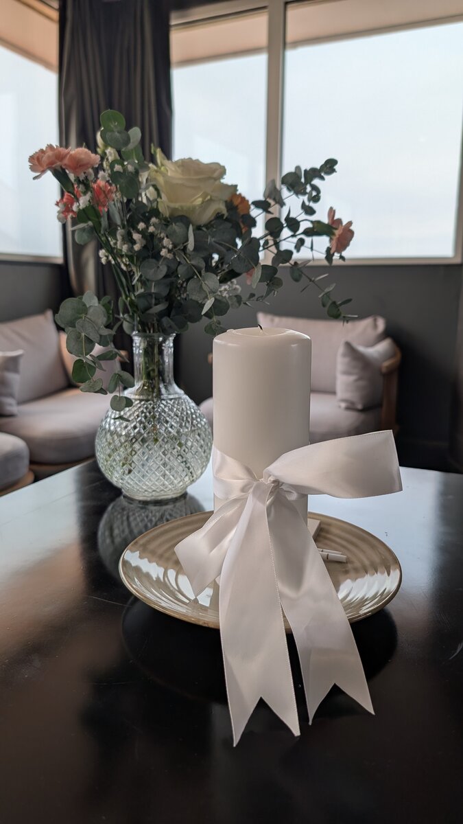 Bougie cérémonielle nouée d'un ruban blanc, accompagnée d'un bouquet de fleurs